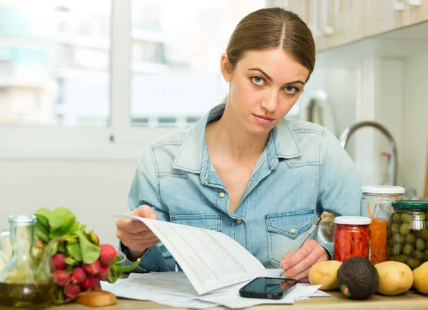 Женщина считает деньги на оплату счетов на кухне — стоковое фото
