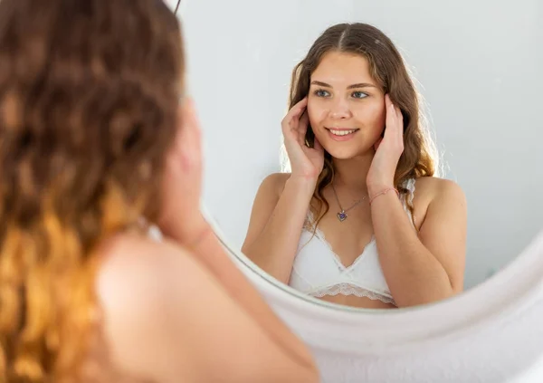 Wanita yang menarik memeriksa wajah di cermin di pagi hari — Stok Foto