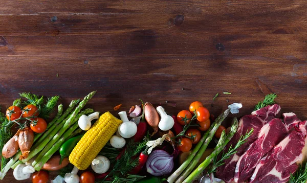 Trozos de carne fresca de res en un escritorio de madera con verduras —  Fotos de Stock