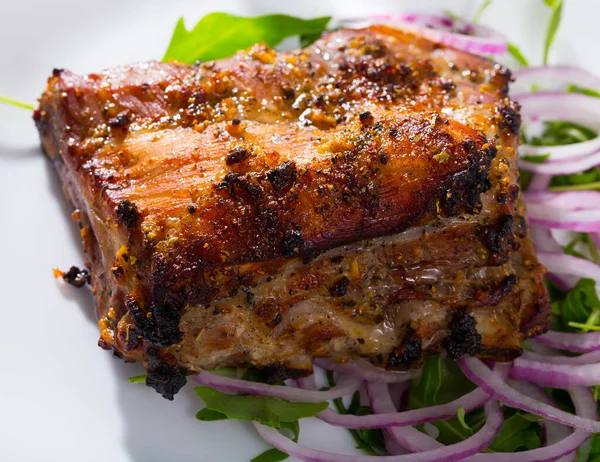 Baked under sauce tasty pork ribs at plate with arugula and onion — Stock Photo, Image