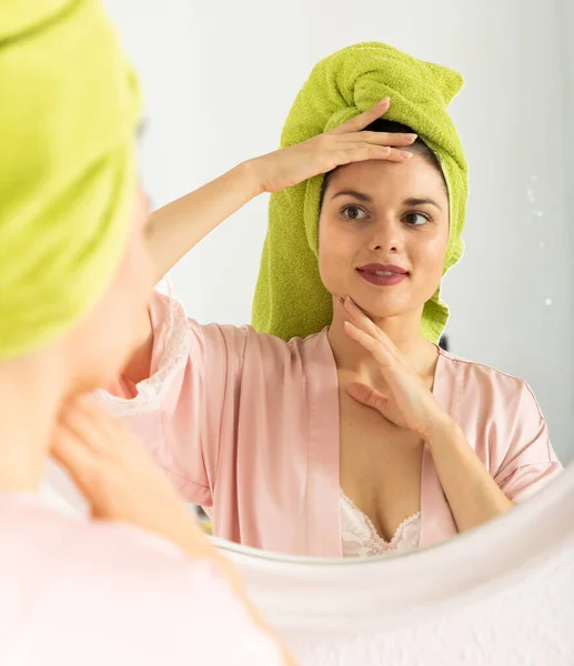 Donna con asciugamano sulla testa vicino allo specchio e al viso toccante — Foto Stock