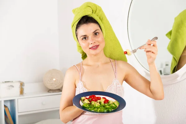Женщина с полотенцем на голове держит вилку, ест овощной салат — стоковое фото