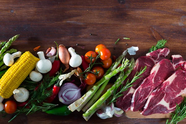 Trozos de carne fresca de res en un escritorio de madera con verduras —  Fotos de Stock
