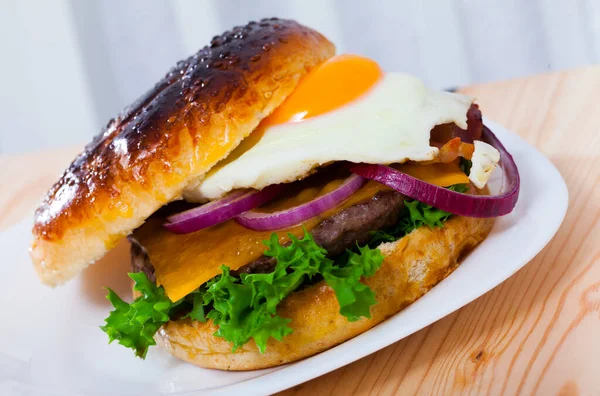 Pyszny hamburger z kotletem wołowym, jajkiem smażonym, sałatą i serem — Zdjęcie stockowe