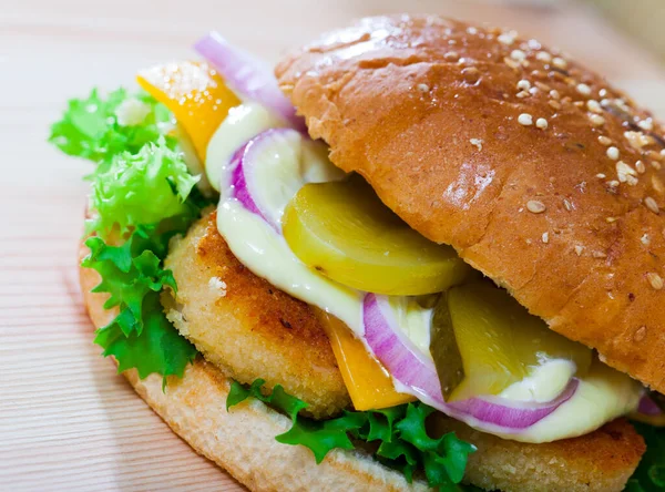Zdjęcie burgera z kotletem z kurczaka, ogórkiem, sałatą i cebulą — Zdjęcie stockowe