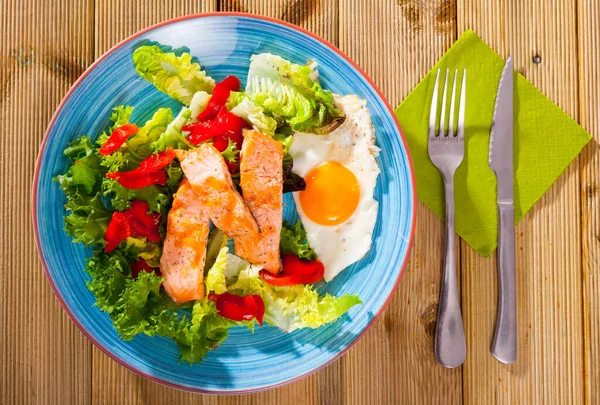 Sabroso desayuno con trucha, huevo, pimienta y lechuga en el plato en la mesa — Foto de Stock