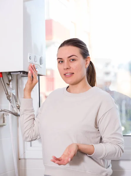 Домохозяйка стоит возле газовой колонны и контролирует температуру воды — стоковое фото