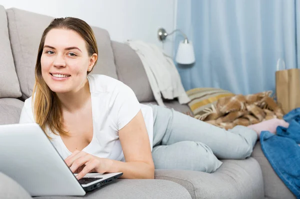 Retrato de mulher alegre que está trabalhando com laptop no sofá — Fotografia de Stock
