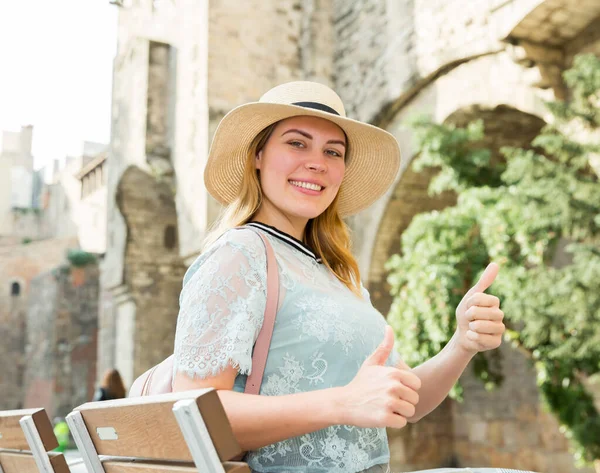 Kvinna turist i hatt nära bänk håller tummen upp i historiska stadskärnan — Stockfoto