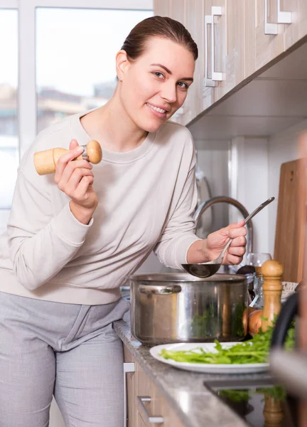 Молодая женщина готовит суп и соль его на кухне — стоковое фото