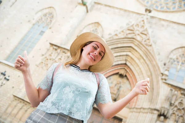 Joven mujer emocional en sombrero sosteniendo pulgares en el centro de la ciudad — Foto de Stock