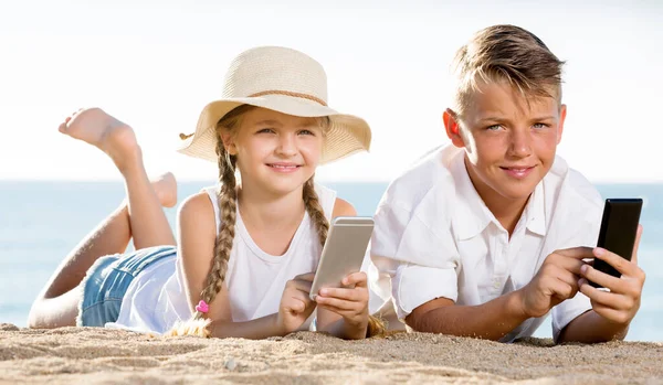 Kumsalda ellerinde telefonla gülümseyen çocuklar. — Stok fotoğraf