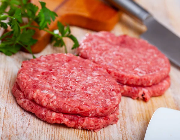 Raw meat cutlets with parsley on wooden board — Stock Photo, Image