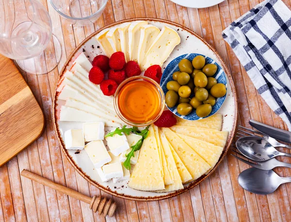Placa con diferentes tipos de queso, frambuesas y aceitunas — Foto de Stock
