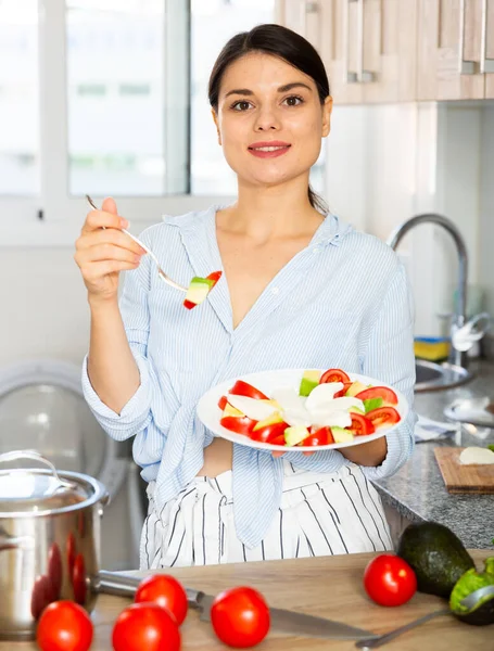 Frau probiert Gemüsesalat in Küche — Stockfoto