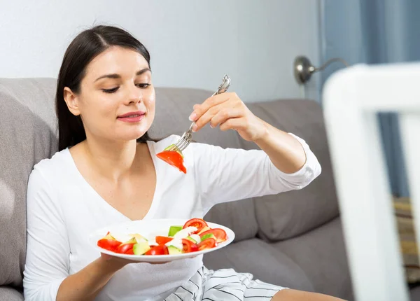 Mulher satisfeita sentada no sofá em casa e comendo alimentos saudáveis — Fotografia de Stock