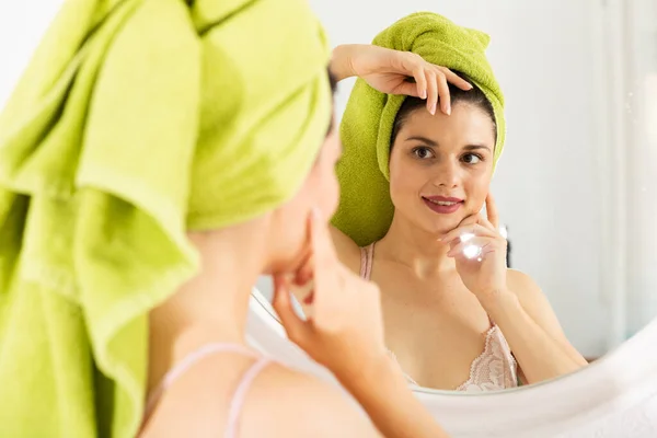 Mädchen mit Handtuch auf dem Kopf berührt Gesicht und schaut in Spiegel — Stockfoto