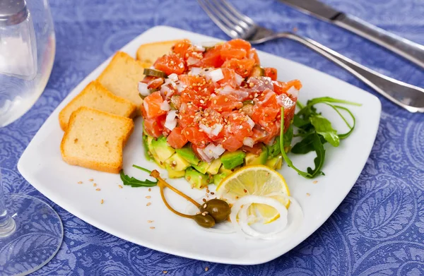 Salmon tartare with avocado served with toasts, arugula, lemon and capers — Stock Photo, Image