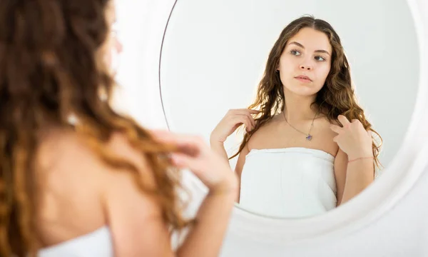 Chica con una toalla en la cabeza se mira en el espejo —  Fotos de Stock