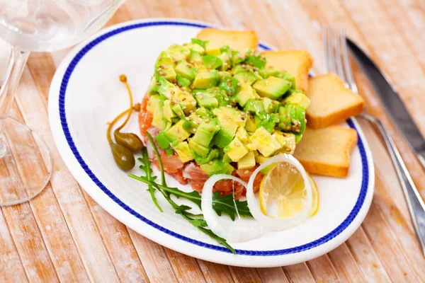 Lax tartar med avokado serveras med rostat bröd, grönt, citron och kapris — Stockfoto
