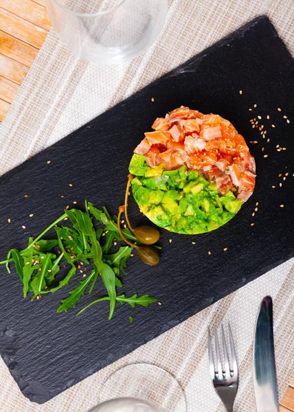 Tartare di salmone con avocado servito con capperi e rucola su tavola di ardesia — Foto Stock