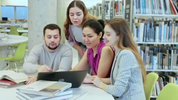Groupe de jeunes femmes adultes positives et d'hommes apprenant ensemble à la bibliothèque, travaillant avec un ordinateur portable et des livres et souriant — Video