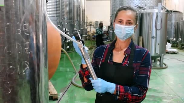 Vrouwelijke werknemer werkt in een wijnmakerij en filtert wijn in vaten — Stockvideo