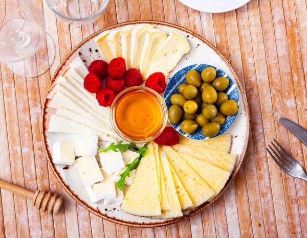 Piatto con diversi tipi di formaggio, lamponi e olive — Foto Stock