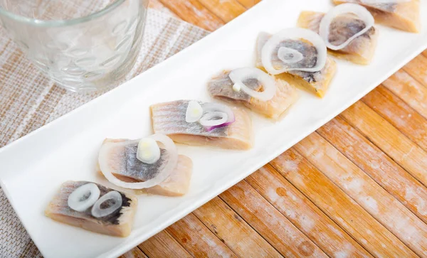 Tahta masada soğanla servis edilen dilimlenmiş ringa balığı. — Stok fotoğraf
