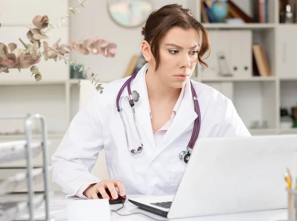 Retrato de médico feminino que está trabalhando com laptop e documentos — Fotografia de Stock