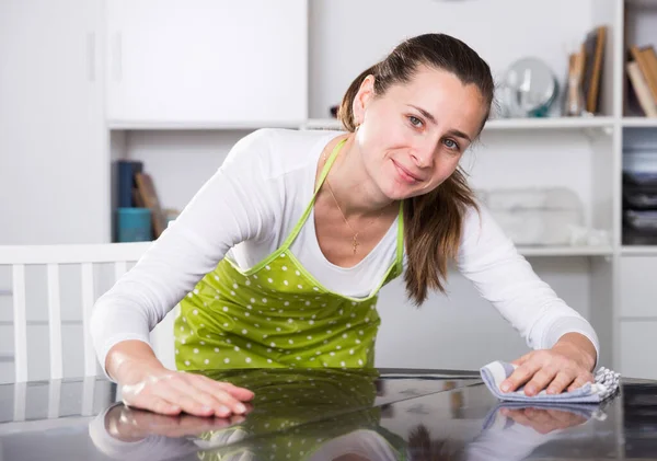 앞치마를 입은 젊은 여자가 집 의식 탁을 청소 한다 — 스톡 사진