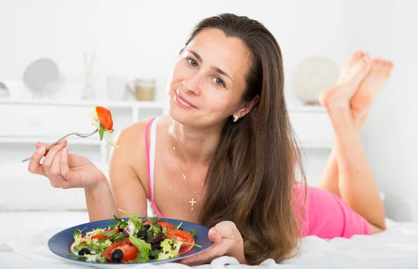 Kvinnan i nattlinne kappa äter sallad i sängen — Stockfoto