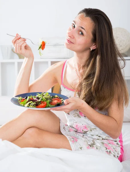 Kvinna äter en aptitretande sallad i sängen — Stockfoto