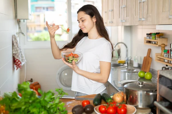 Young woman eating vegetable salad in kitchen — Stock Photo, Image