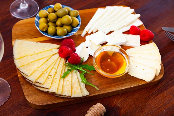Piatto con diversi tipi di formaggio, lamponi e olive — Foto Stock