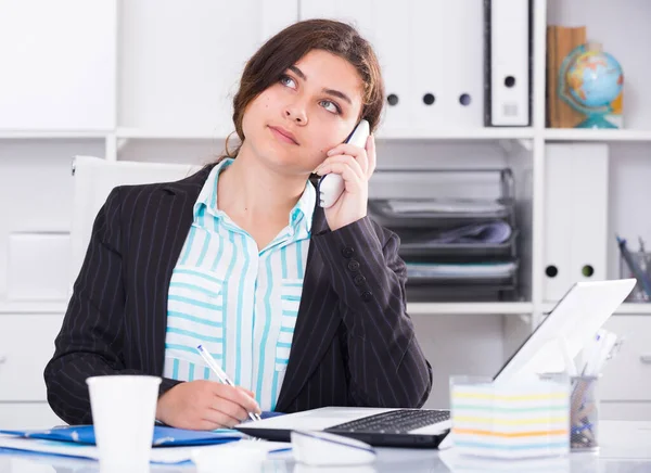 Young female trainee is working at a computer and talking phone — Stock Photo, Image