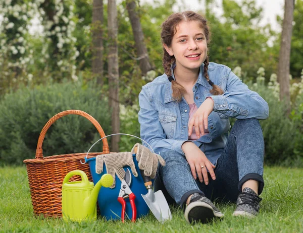 Adolescente con attrezzi da giardinaggio seduto sull'erba in giardino — Foto Stock