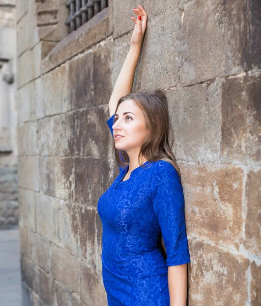 Vidám nő játékosan pózol kék ruhában a fal mellett. — Stock Fotó