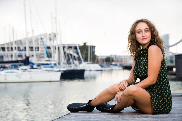 Joven chica sexy turista en vestido juguetonamente posando en el muelle con barcos —  Fotos de Stock