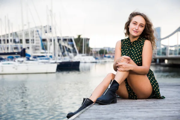 Sexy dziewczyna w sukience siedzi na nabrzeżu z łodzi na tle w Barcelonie — Zdjęcie stockowe