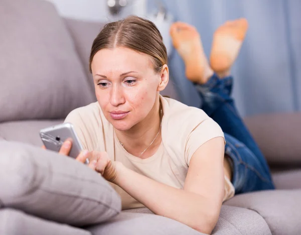 Стурбована жінка на дивані з телефоном — стокове фото