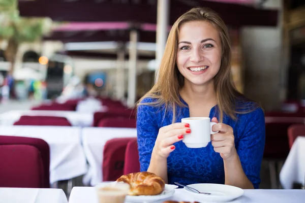 Mladá žena obědvá s croissantem a kávou — Stock fotografie