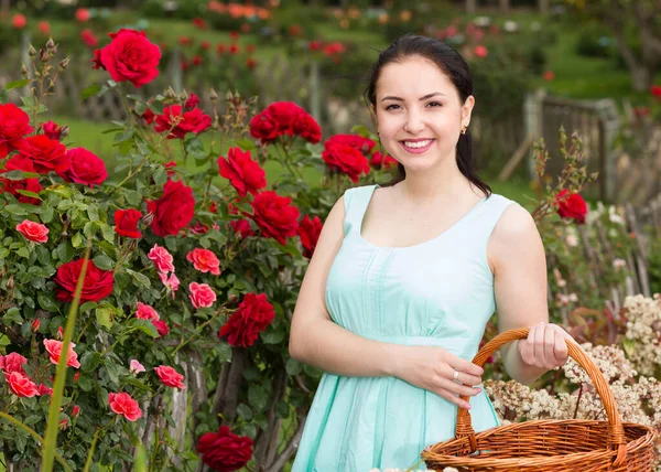 Retrato de jovem fêmea segurando uma cesta perto de rosas ao ar livre — Fotografia de Stock