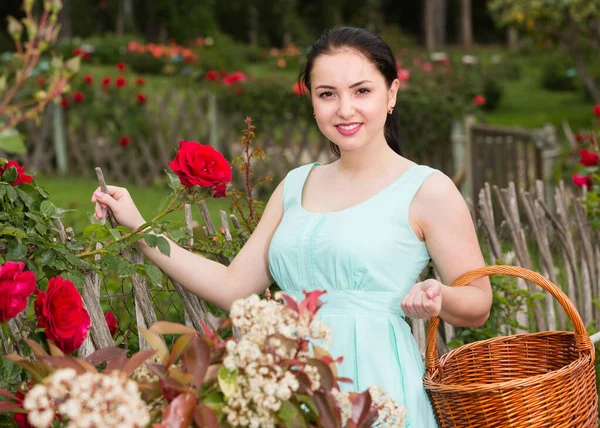 Retrato de jovem fêmea segurando uma cesta perto de rosas ao ar livre — Fotografia de Stock