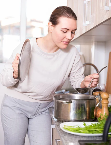 快乐的女性站在餐桌旁 在厨房里端着盛着汤和盐的锅 — 图库照片