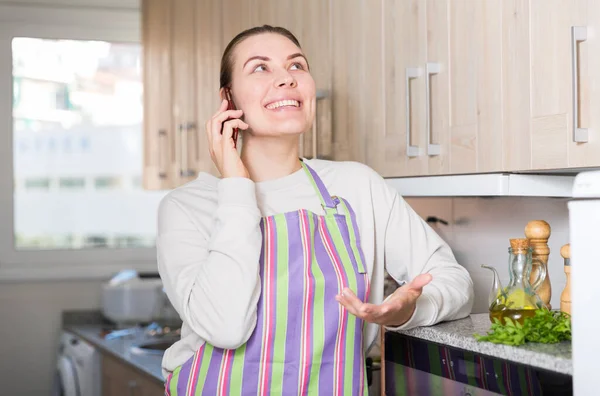 家庭主妇拿着电话站在自家厨房里和丈夫说话 — 图库照片