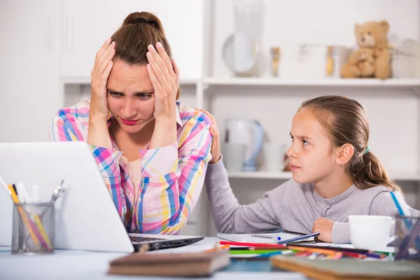 Portrait of sad female with little schoolgirl doing homewor