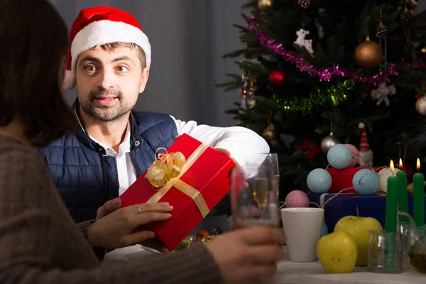 夕食で新年を祝う若いカップル帽子の男は女性にプレゼントを与える — ストック写真