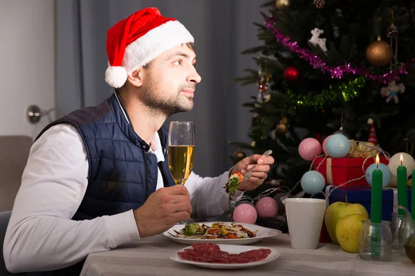 帽子の若い男性はシャンパンで新年を祝い 自宅のインテリアでテレビを見て — ストック写真