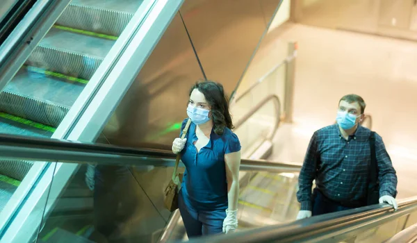 Focused people in medical masks and rubber gloves lifting on escalator keeping distance to prevent spread of COVID 19 virus. High quality photo